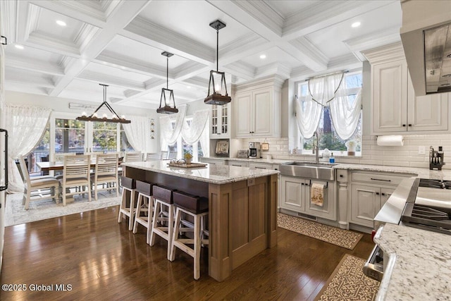 kitchen featuring dark wood-style flooring, light stone counters, beam ceiling, decorative backsplash, and a kitchen island