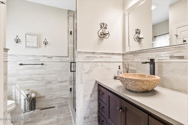 full bathroom with visible vents, a stall shower, vanity, a wainscoted wall, and toilet