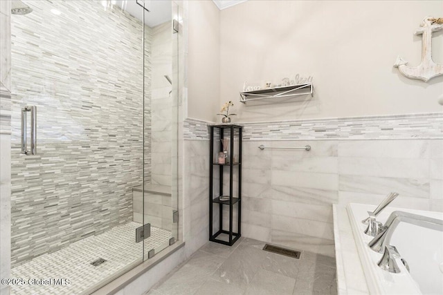 bathroom featuring visible vents, tile patterned flooring, tile walls, a tub to relax in, and a stall shower