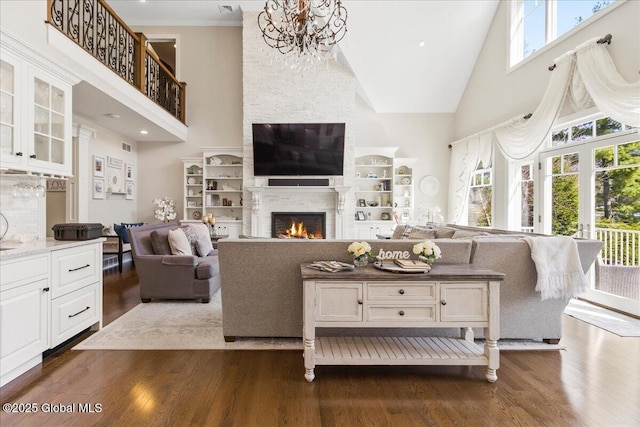living area featuring high vaulted ceiling, a warm lit fireplace, dark wood-style floors, and a notable chandelier