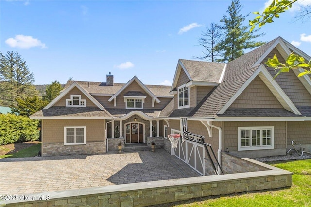 view of front of home with a chimney, a shingled roof, and stone siding
