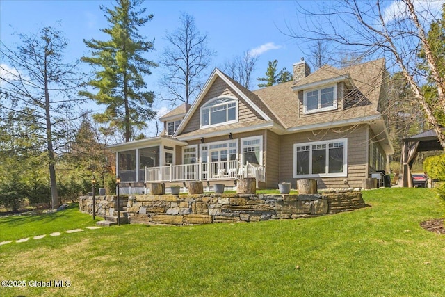 rear view of house with a yard, roof with shingles, a chimney, and a sunroom