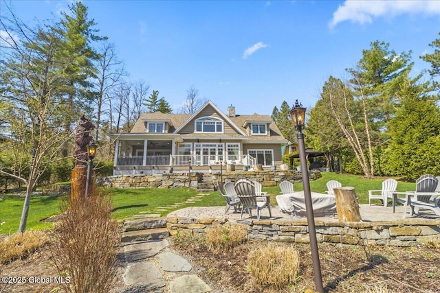 rear view of house featuring a sunroom, a yard, a patio area, and an outdoor fire pit