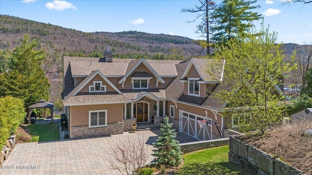 view of front facade featuring a chimney, a garage, a gazebo, a shingled roof, and stone siding