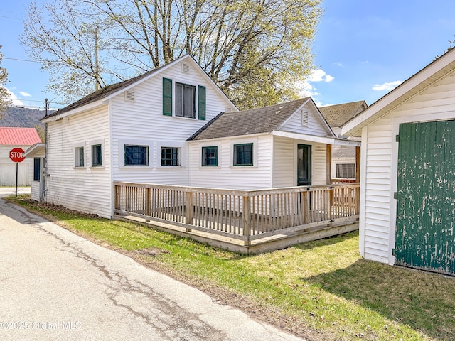 view of front of property with a wooden deck, a shingled roof, and a front lawn