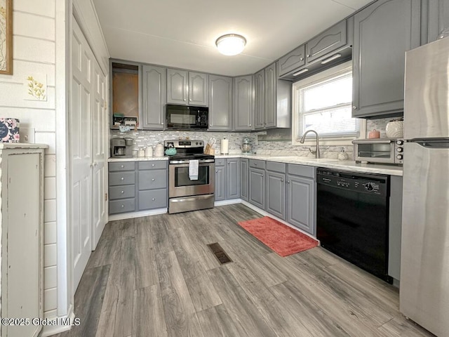 kitchen with gray cabinets, wood finished floors, black appliances, a sink, and visible vents