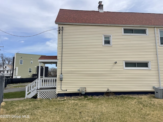 view of side of property with a lawn, a chimney, and central AC