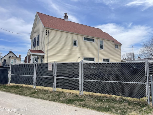 view of home's exterior with a chimney, fence, and roof with shingles