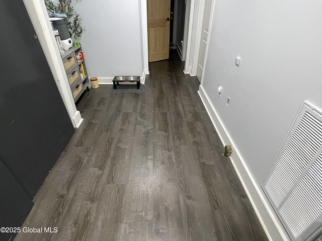 hallway with dark wood finished floors, visible vents, and baseboards