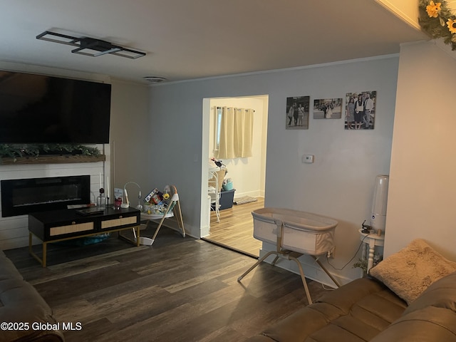 living room featuring a glass covered fireplace, wood finished floors, crown molding, and baseboards