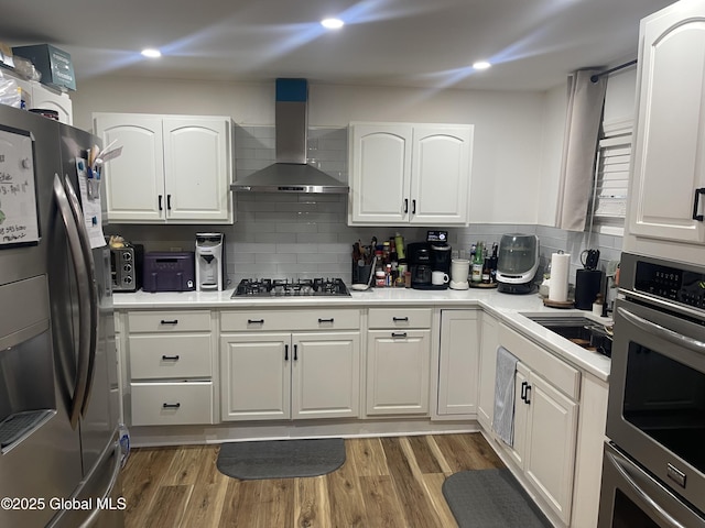 kitchen featuring wall chimney range hood, oven, gas stovetop, white cabinetry, and refrigerator with ice dispenser