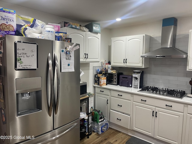 kitchen featuring white cabinets, stainless steel appliances, wood finished floors, wall chimney range hood, and light countertops