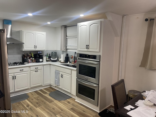 kitchen with backsplash, wall chimney range hood, white cabinets, and stainless steel appliances