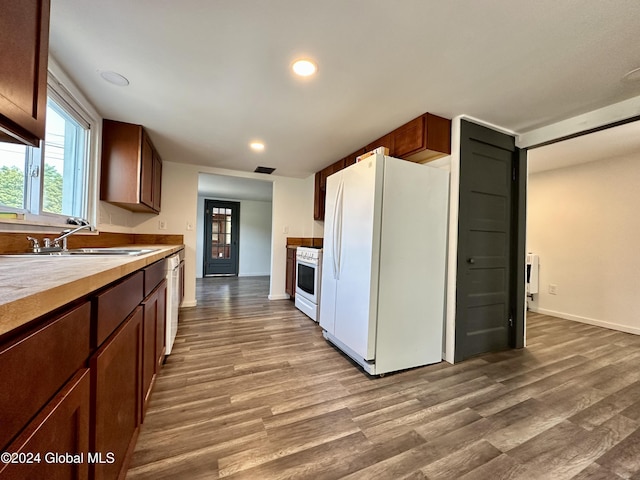 kitchen with wood finished floors, baseboards, a sink, and white appliances
