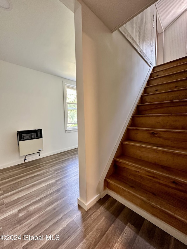 stairs with wood finished floors, baseboards, and heating unit