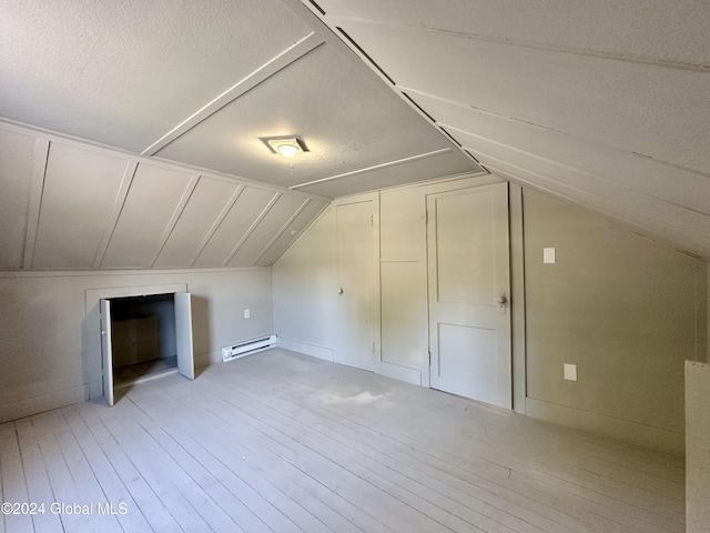 additional living space featuring a baseboard radiator, lofted ceiling, a textured ceiling, and light wood-type flooring
