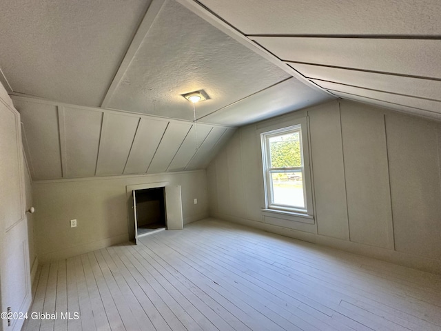 additional living space featuring lofted ceiling, hardwood / wood-style floors, and a textured ceiling