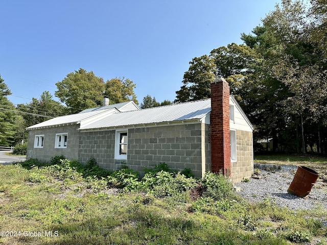 view of side of property with a chimney, concrete block siding, and metal roof