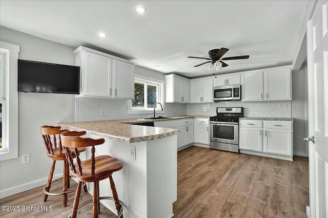 kitchen featuring white cabinets, stainless steel appliances, a peninsula, a sink, and backsplash
