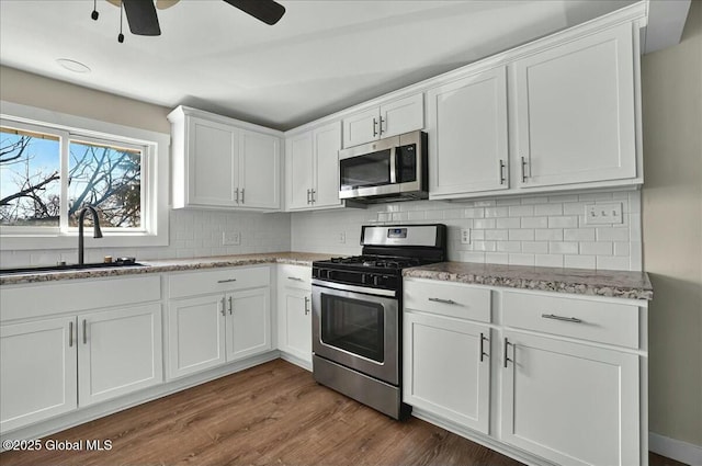 kitchen with stainless steel appliances, white cabinetry, a sink, decorative backsplash, and ceiling fan