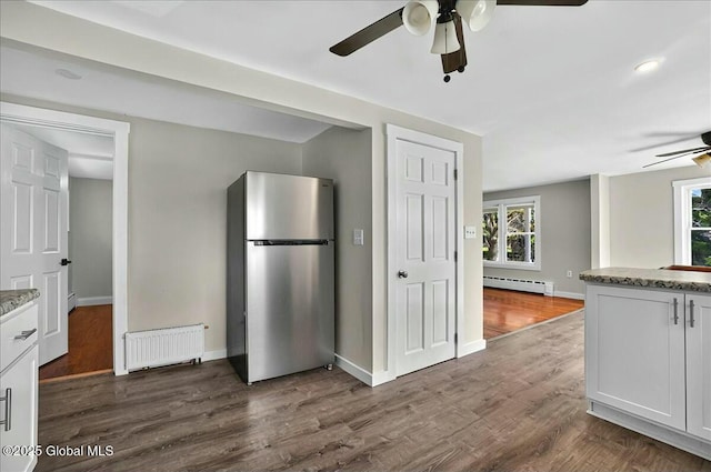 kitchen with a baseboard heating unit, ceiling fan, radiator, dark wood-style floors, and freestanding refrigerator