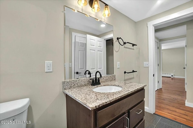 bathroom with a baseboard heating unit, toilet, baseboards, wood finished floors, and vanity