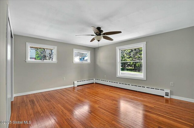 empty room with baseboard heating, wood-type flooring, baseboards, and a ceiling fan