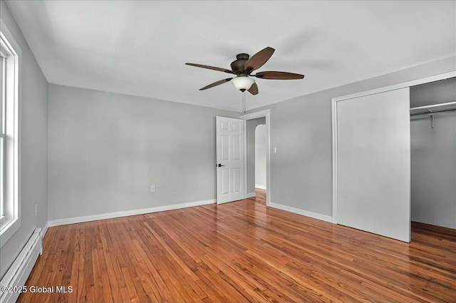 unfurnished bedroom with arched walkways, baseboards, baseboard heating, a closet, and wood-type flooring