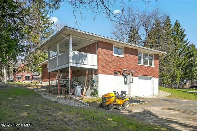 rear view of property with driveway, a ceiling fan, an attached garage, brick siding, and stairs