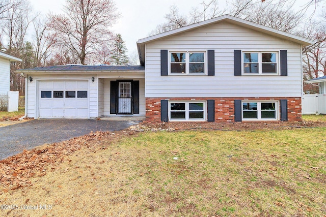 split level home with an attached garage, a front lawn, aphalt driveway, and brick siding