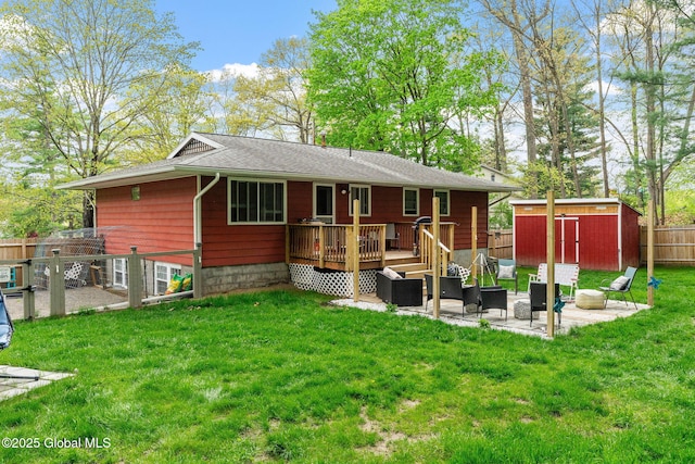 back of house with a deck, a patio area, an outdoor structure, a shed, and roof with shingles