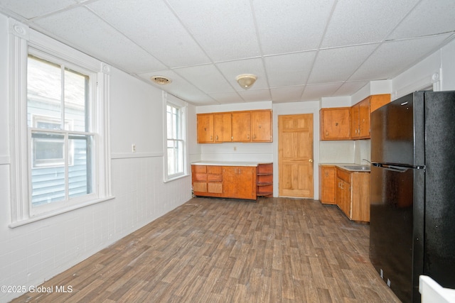 kitchen with a sink, brown cabinetry, freestanding refrigerator, dark wood-style flooring, and a drop ceiling