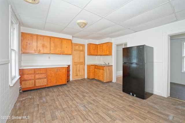 kitchen featuring freestanding refrigerator, dark wood finished floors, a sink, a paneled ceiling, and brown cabinets