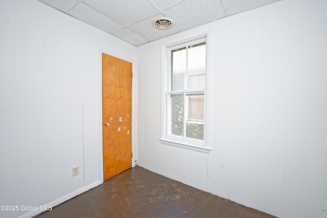 unfurnished room with a paneled ceiling, concrete floors, a decorative wall, and visible vents