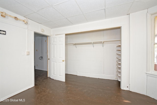 unfurnished bedroom with a paneled ceiling, baseboards, a closet, and wood finished floors