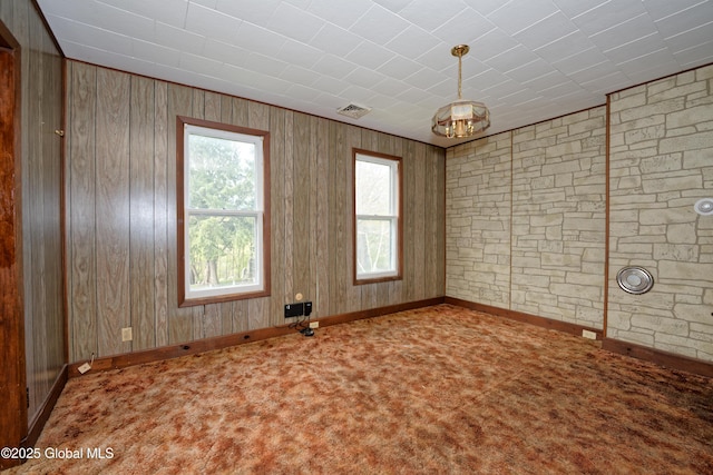 carpeted spare room featuring baseboards, wooden walls, and visible vents