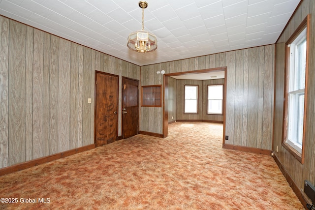 unfurnished room featuring an inviting chandelier, wood walls, carpet flooring, and baseboards