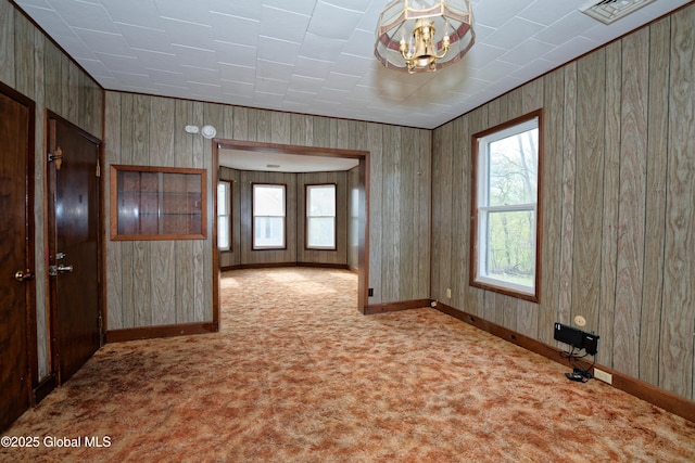 carpeted spare room featuring wood walls, visible vents, baseboards, and a notable chandelier