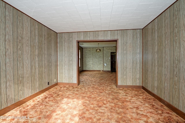 empty room with wood walls, baseboards, and carpet floors