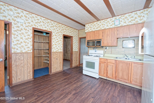 kitchen with white range with gas stovetop, a sink, wallpapered walls, dark wood-type flooring, and wainscoting