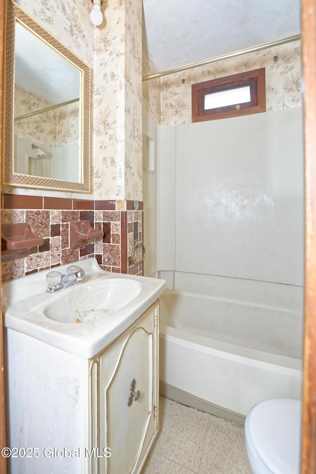 bathroom with toilet, vanity, bathtub / shower combination, and wallpapered walls