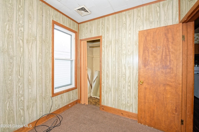 unfurnished bedroom featuring wood walls, multiple windows, ornamental molding, visible vents, and carpet flooring
