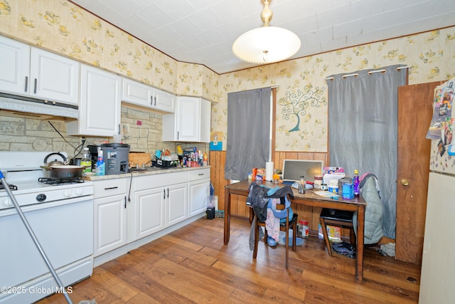 kitchen featuring under cabinet range hood, wallpapered walls, wood finished floors, and white appliances