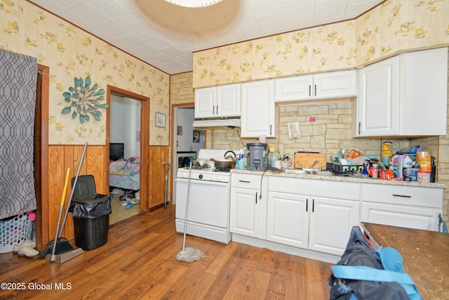 kitchen with light wood finished floors, wallpapered walls, wainscoting, under cabinet range hood, and gas range gas stove
