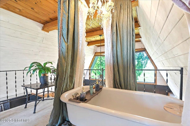 full bathroom with beamed ceiling, wood walls, wooden ceiling, a freestanding tub, and wood finished floors