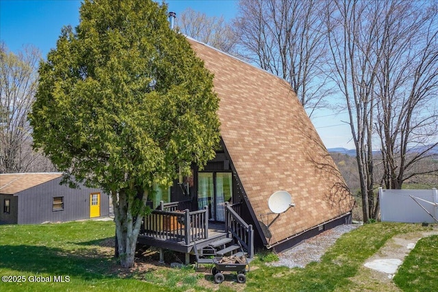 back of property featuring fence, roof with shingles, a deck, and a lawn