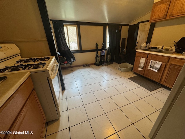 kitchen with brown cabinets, light tile patterned floors, white range with gas cooktop, and a sink