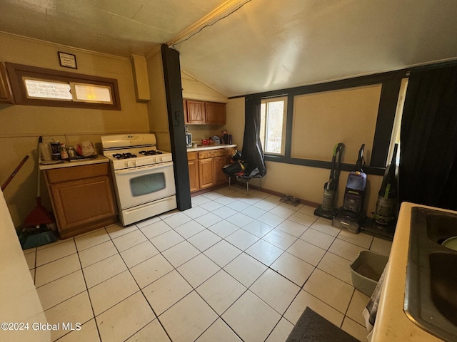 kitchen with white gas range, brown cabinets, light tile patterned flooring, light countertops, and lofted ceiling