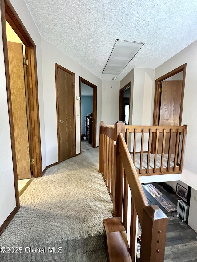 hall featuring an upstairs landing, a textured ceiling, carpet, baseboards, and attic access