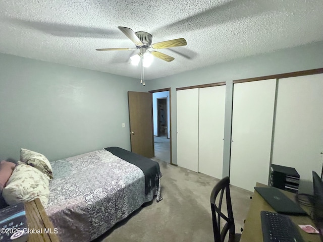 bedroom featuring two closets, light carpet, ceiling fan, and a textured ceiling